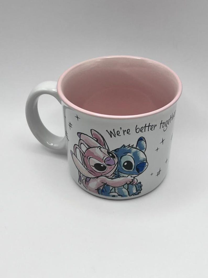 May include: White ceramic mug with a pink interior and handle. The mug features a cartoon illustration of two characters hugging, with the text "We're better together" and star accents.