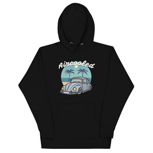 Könnte beinhalten: Ein schwarzer Kapuzenpullover mit einem Grafikdruck eines hellblauen Oldtimers. Das Design zeigt einen kreisförmigen Hintergrund mit Palmen, einem Strand und der Sonne, wobei der Text Aircooled in weißer Schreibschrift darüber steht.
