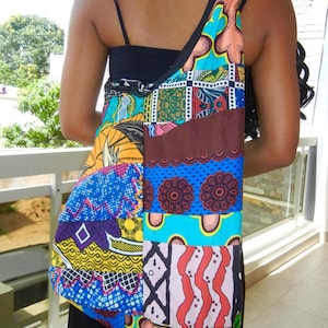 May include: A vibrant patchwork shoulder bag featuring a mix of patterns and colours, such as blue, yellow, orange, and brown. The bag has a broad strap and is worn over the shoulder. The bag is made of fabric.