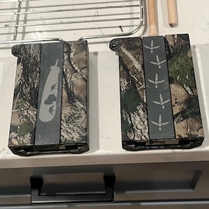May include: Two rectangular knife sharpeners with a camouflage pattern. One has a feather design, the other has a bird footprint design. Both have a dark gray center section.