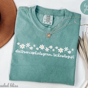 May include: A light green t-shirt with a white daisy border and the text "electroencephalogram technologist" in white.
