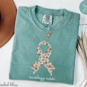 May include: Light green t-shirt with a floral patterned ribbon and the text "oncology nurse".