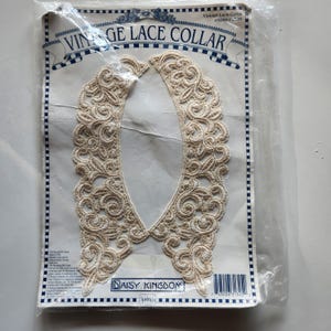 May include: A vintage lace collar in a cream color with a delicate floral pattern. The collar is packaged in a plastic bag with a label that reads "Vintage Lace Collar" and "Daisy Kingdom".