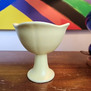 Può includere: Un vaso in ceramica giallo pallido con una ciotola larga e arrotondata e uno stelo alto e sottile. Il vaso ha una finitura liscia e lucida.