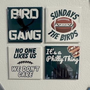 May include: Four square green and white refrigerator magnets with different designs and sayings. The first magnet says "Bird Gang" with a black eagle. The second magnet says "Sundays are for the Birds" with a football. The third magnet says "No One Likes Us We Don't Care" with a football stitch. The fourth magnet says "It's a Philly Thing" with a skyline and a cheesesteak.