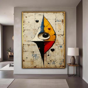 May include: Abstract artwork in a gold frame. The piece displays a geometric design on a white background, with a central shape in yellow, blue, red, and black. Black circular accents are scattered across the surface.