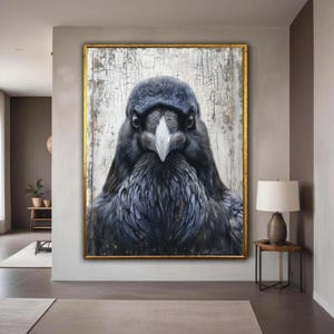 May include: A framed painting of a raven, predominantly black and grey with a white beak. The artwork has a distressed white background and a gold frame. The painting is displayed in a modern interior setting, creating a striking visual contrast.