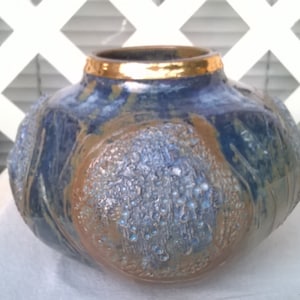 May include: A blue and brown ceramic vase with a gold rim. The vase has a textured surface and a unique design.