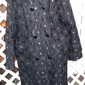May include: A black double-breasted coat with a floral pattern and large black buttons. The coat features a notched collar and two front pockets. Small, round, gold-colored accents are scattered across the fabric.