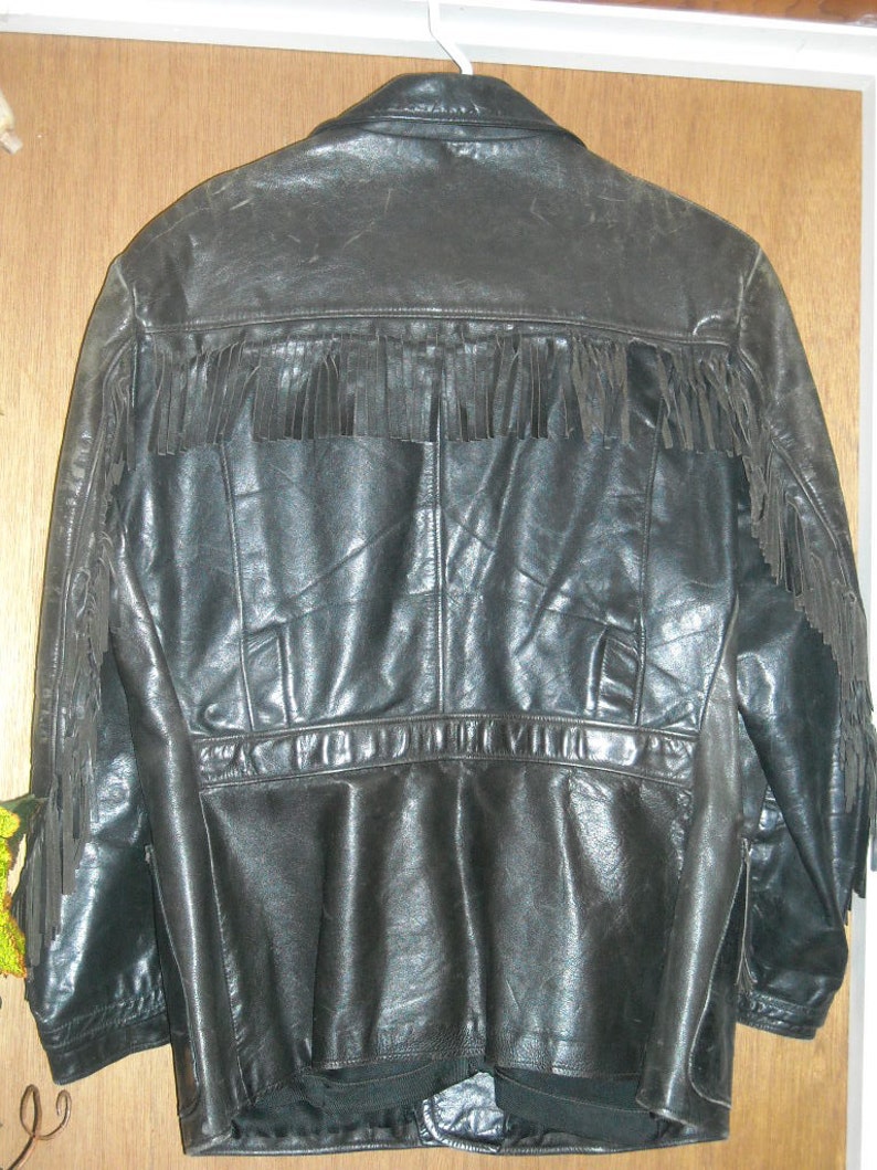Pode incluir: Uma jaqueta de couro preta com detalhes de franjas nos ombros e na bainha inferior. A jaqueta tem um fecho de correr e v&aacute;rios bolsos.