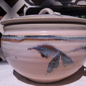 May include: A ceramic soup tureen with a lid. The tureen is a light pink color with blue and brown accents. It has a handle on each side and a handle on the lid. The tureen is approximately 10 inches in diameter.