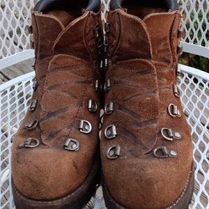 May include: A pair of brown leather hiking boots with a tiger stripe pattern. The boots have metal buckles and a thick rubber sole.