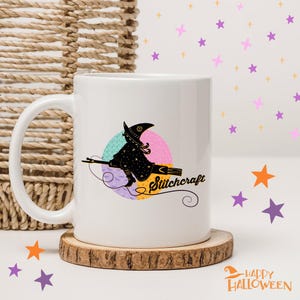 Può includere: Tazza in ceramica bianca con una silhouette di strega nera su una scopa, e la parola "Stitchcraft". La tazza è su un sottobicchiere di legno, a tema Halloween.
