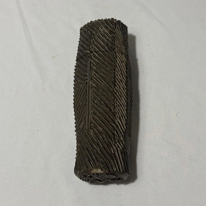 May include: A dark brown, rectangular object with a textured surface. The object has a series of diagonal lines carved into it, creating a pattern. The object is standing upright on a white surface.