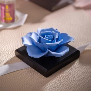May include: A light blue ceramic rose on a black square base. The rose is a decorative item for the home.