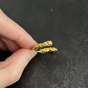 May include: A gold ring with a detailed, intricate design. The ring is open and has a twisted, rope-like appearance.