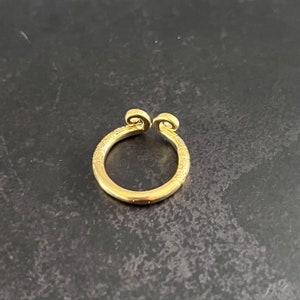 May include: A gold ring with a unique design featuring two curled ends. The ring is made of metal and has a smooth, polished finish.