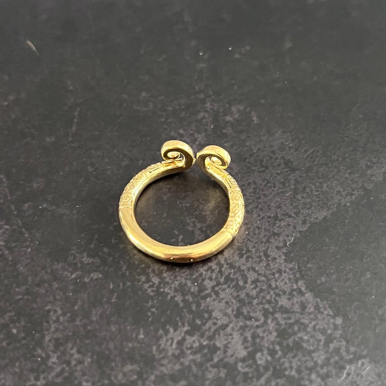May include: A gold ring with a unique design featuring two curled ends. The ring is made of metal and has a smooth, polished finish.