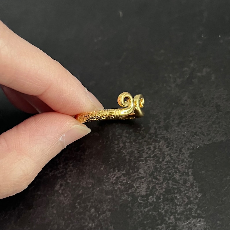 May include: A gold ring with a detailed, ornate design. The ring features a unique, curled design on the top.