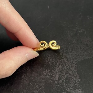 May include: A gold ring with two curled designs on the top. The ring is simple and elegant.