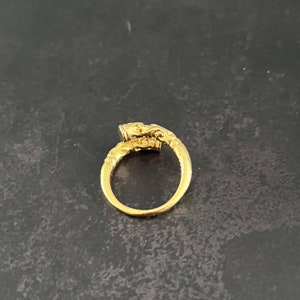 May include: A gold ring with an ornate design. The ring has a large, oval-shaped stone set in the center.