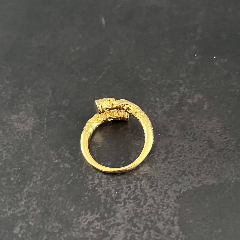 May include: A gold ring with an ornate design. The ring has a large, oval-shaped stone set in the center.