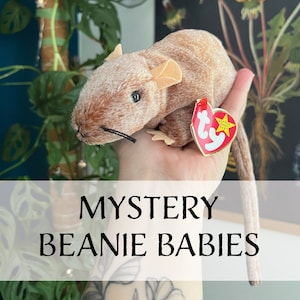 May include: A brown and white plush rat beanie baby with a red Ty tag that says "Beanie Baby" on it. The beanie baby is being held in a hand with a tattoo.