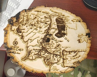 Puede incluir: Una rodaja de madera con un mapa de la Tierra Media quemado, de El Señor de los Anillos. El mapa incluye los nombres de lugares como Mordor, Rohan y Forodwaith.