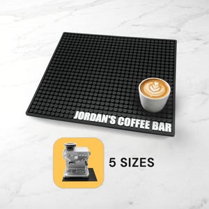 Puede incluir: Una alfombrilla de café rectangular de goma negra con una superficie de rejilla texturizada y el texto blanco JORDAN'S COFFEE BAR. Una taza de cerámica blanca con arte latte se asienta sobre la alfombrilla. Un recuadro muestra una cafetera y 5 SIZES.