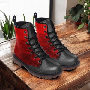 May include: A pair of black and red combat boots with black laces. The boots have a textured design on the red upper and black lower sections. The boots are displayed on a wooden surface.