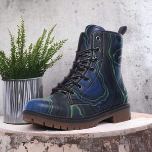 May include: A striking combat boot with a marbled pattern in blue and green. It has black laces, eyelets, and a pull tab. The sole is brown. The boot is displayed against a neutral backdrop with a small potted plant.