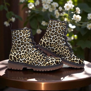 May include: A pair of ankle boots with a leopard print pattern. The boots have black laces, black trim, and brown soles. The boots are displayed on a brown table with a blurred background of white flowers and green foliage.