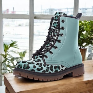 May include: A teal and black leopard print combat boot with black laces. The boot has a teal upper and a brown sole. The boot is sitting on a wooden surface. The boot is a fashion item.