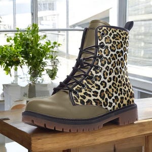 May include: An olive green and leopard print combat boot with black laces. The boot features a brown sole and a pull tab at the back. The leopard print is a mix of tan and brown spots.
