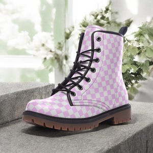 May include: A pink and white chequered combat boot with black laces and a brown sole. The boot has a round toe and a small heel. The boot is made of a synthetic material and has a black trim.