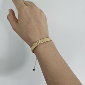 Puede incluir: Una pulsera dorada con un dise&ntilde;o de cuentas. La pulsera se lleva en la mu&ntilde;eca y tiene una cadena ajustable. El dise&ntilde;o est&aacute; hecho de peque&ntilde;as cuentas redondas, creando una superficie texturizada. El fondo es blanco liso.