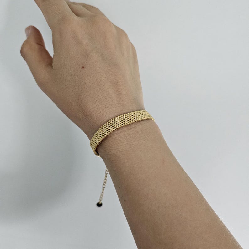 Puede incluir: Una pulsera dorada con un dise&ntilde;o de cuentas. La pulsera se lleva en la mu&ntilde;eca y tiene una cadena ajustable. El dise&ntilde;o est&aacute; hecho de peque&ntilde;as cuentas redondas, creando una superficie texturizada. El fondo es blanco liso.