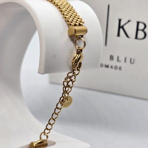 Puede incluir: Pulsera dorada con un dise&ntilde;o de cadena tejida. La pulsera tiene un cierre de mosquet&oacute;n y una cadena ajustable. La imagen muestra la pulsera sobre un expositor blanco. La marca "KB BLIU DMADE" es visible en el fondo.