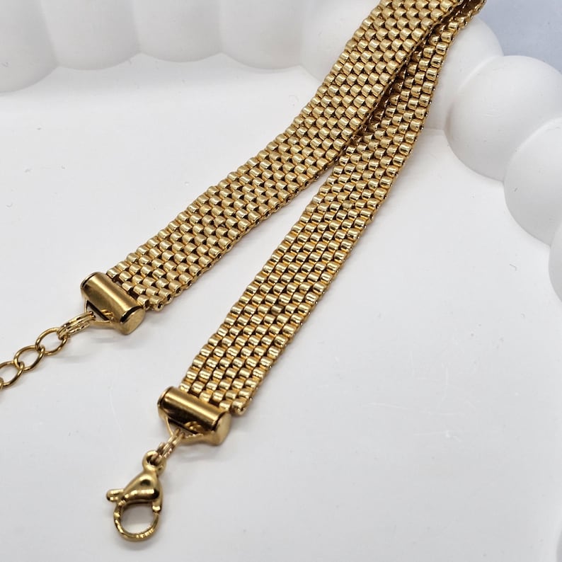 Puede incluir: Collar de metal dorado con un dise&ntilde;o de malla tejida. El collar presenta un cierre de mosquet&oacute;n y una cadena ajustable. El primer plano resalta la intrincada textura y el c&aacute;lido color met&aacute;lico de la joya.