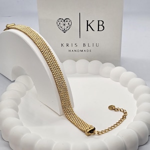 Puede incluir: Una pulsera de malla dorada, exhibida sobre un soporte decorativo blanco. La pulsera tiene forma rectangular con una extensi&oacute;n de cadena. El fondo presenta una caja blanca con un logotipo de coraz&oacute;n y el texto "KB KRIS BLIU HANDMADE."