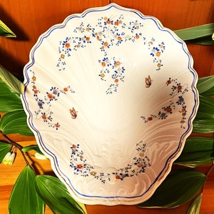 Könnte beinhalten: Eine weiße Keramikschüssel mit gewelltem Rand und einem Blumendesign in Blau-, Orange- und Goldtönen. Die Schüssel ist muschelförmig.