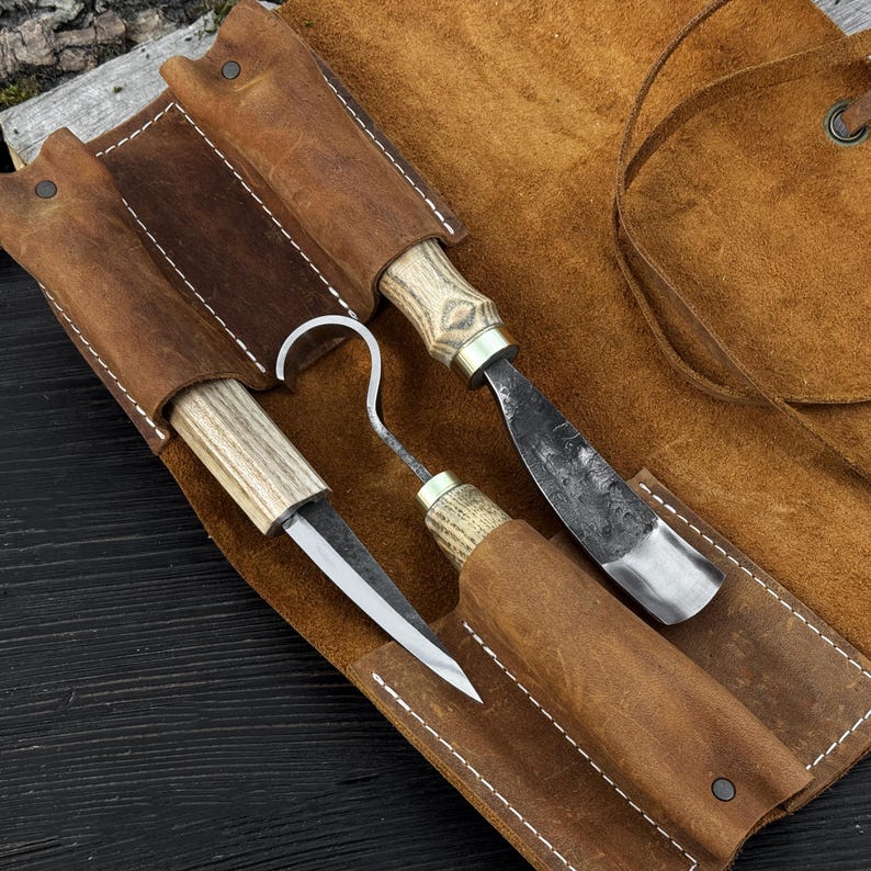 Hand-forged carving tools in open leather roll, spoon carving kit on wooden background.