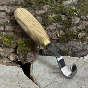 Hand forged hook knife on wood slice and moss, curved blade for shaping bowls, cups and deep spoon interiors in wood.