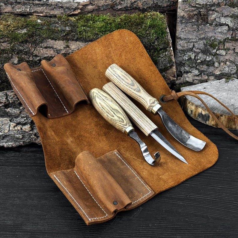 Wood carving kit with leather roll, hook knife, sloyd knife and curved gouge displayed together.
