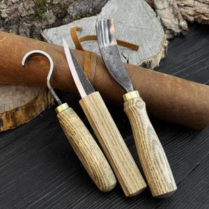 Spoon carving tool set close-up, forged blades and ash handles with leather roll in background.