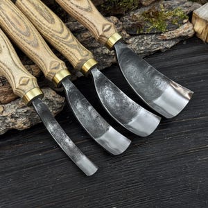 May include: Four wood carving gouges with wooden handles and metal blades. The handles are light brown with a brass ferrule. The curved blades have a silver finish. The tools are displayed on a dark wooden surface.