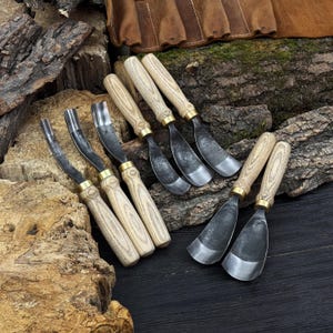 May include: A collection of wood carving tools with wooden handles and metal blades. The tools are arranged on a wooden surface, showcasing their various shapes and sizes. The handles are light-colored, and the blades have a silver finish.