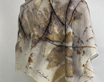 May include: A white silk scarf with a botanical print in shades of brown, beige, and gray. The scarf is folded and draped over a mannequin. The artist's signature, "Laura Baker", is visible in the lower right corner.