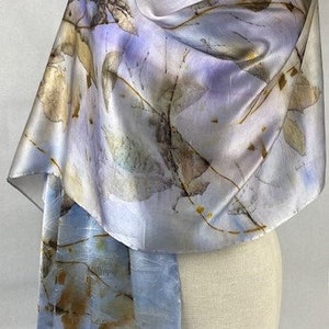 May include: A light blue silk scarf with a delicate pattern of brown and gold leaves. The scarf is draped over a white mannequin.