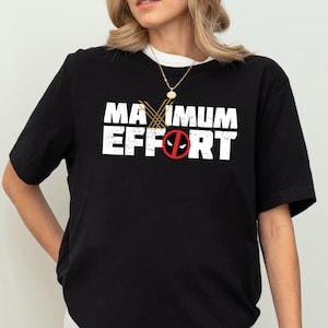 Könnte beinhalten: Schwarzes T-Shirt mit dem weißen Schriftzug "MAXIMUM EFFORT". Das Design beinhaltet ein Deadpool-Logo und Wolverine-Krallen. Lässiger Stil.